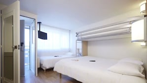 Una habitación de hotel con una cama, una mesita de noche, un televisor montado en la pared y una ventana con cortinas.