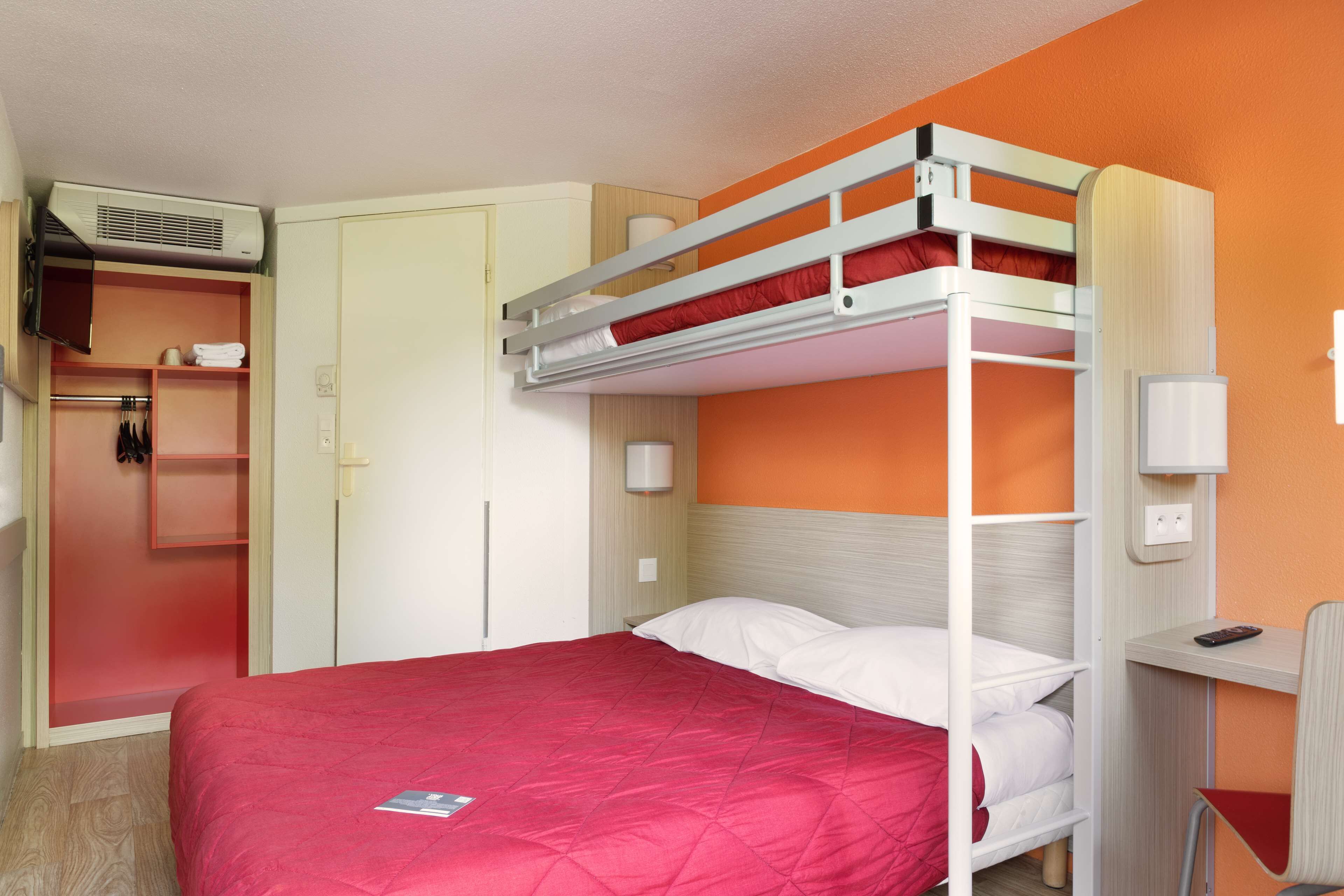 Een stapelbed met een rode matras, een bureau met stoel en een kledingkast met spiegel.