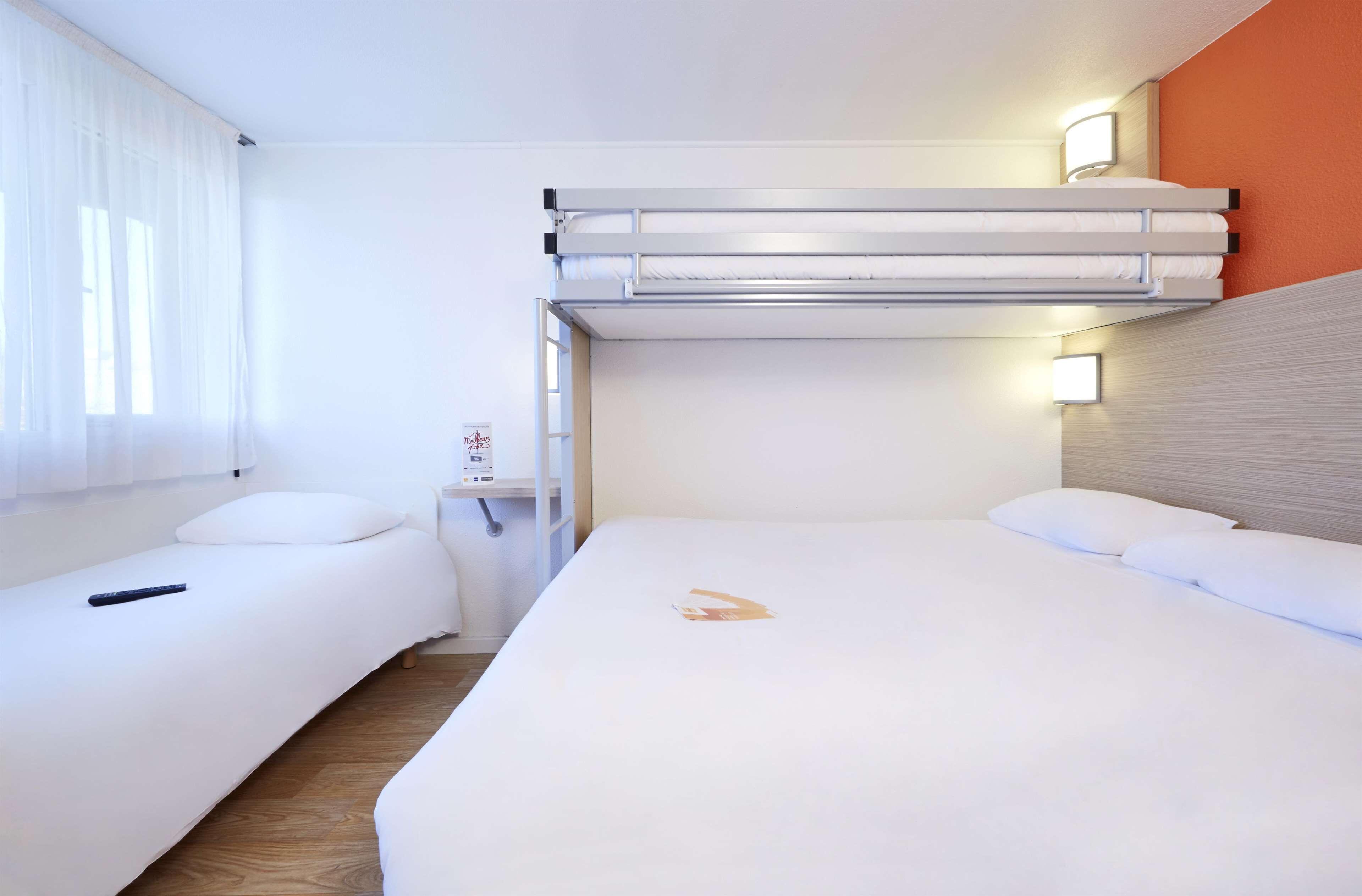 Une chambre d’hôtel avec deux lits, un lit superposé, une table de chevet et une fenêtre avec des rideaux.