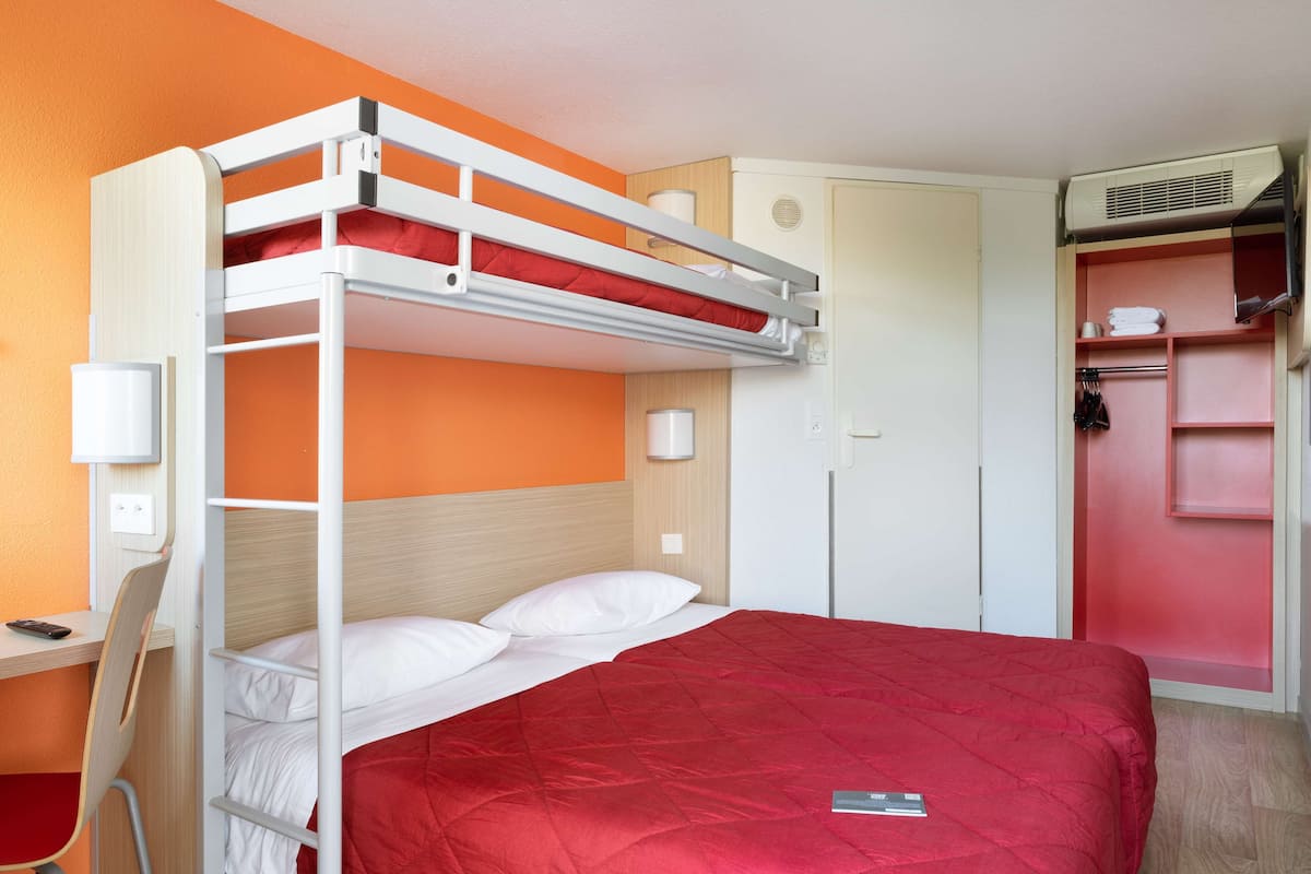 A bunk bed with a red quilt, a desk with a chair, and a wardrobe with a mirror.