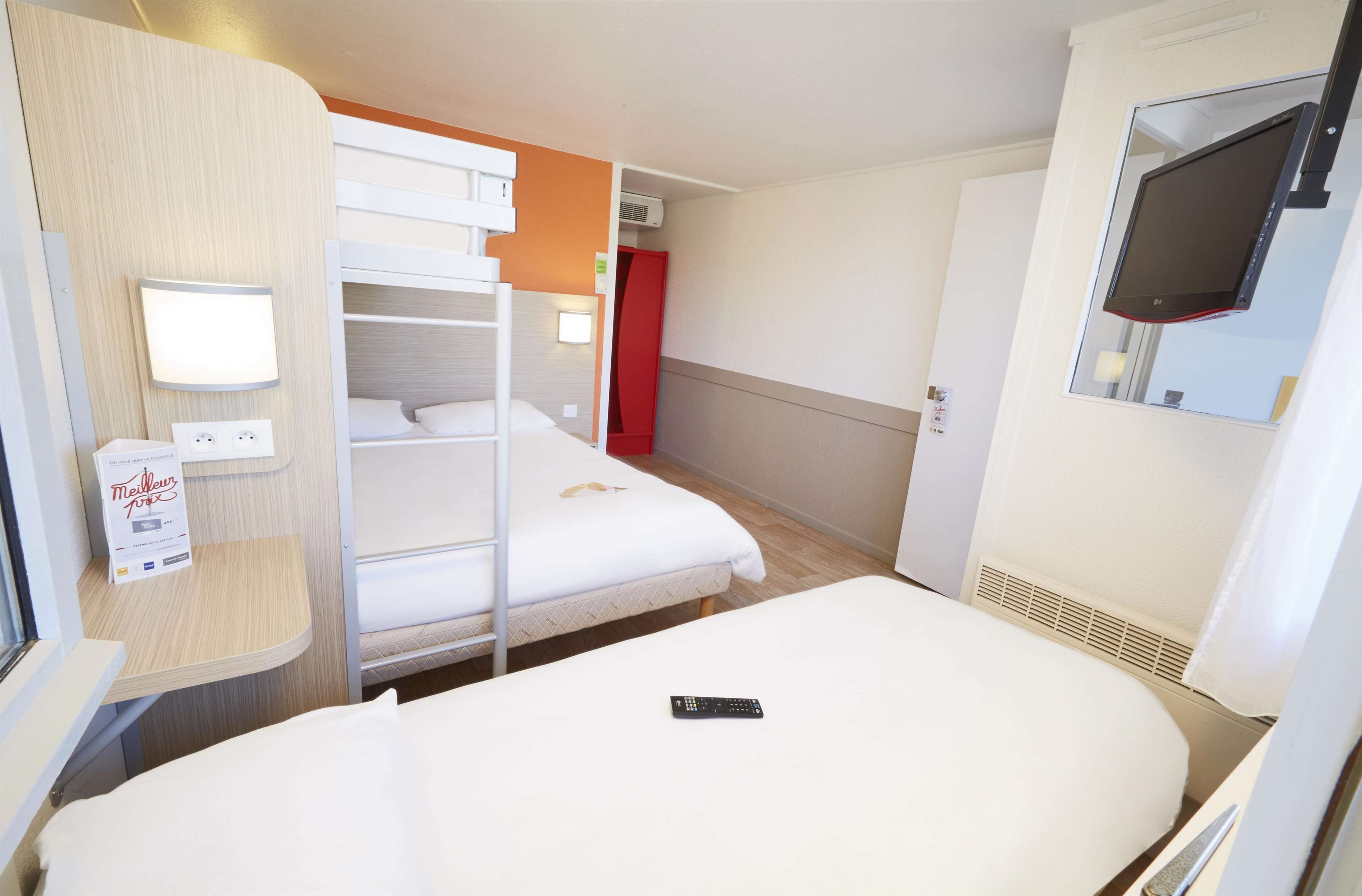 Une chambre d’hôtel équipée d’un lit superposé, d’un lit simple, d’un téléviseur fixé au mur, d’une table de chevet avec une lampe et d’une prise de courant.