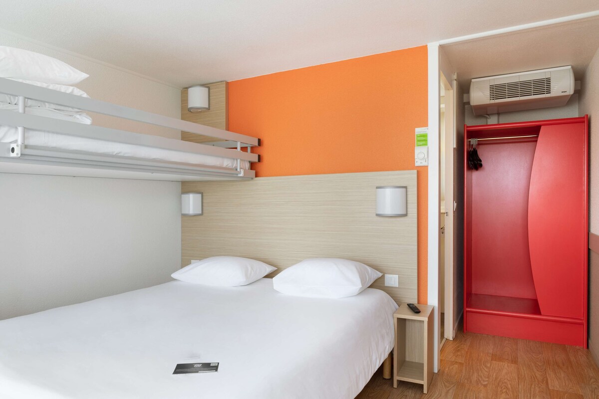 Una cama individual con ropa blanca, cabecera de madera y un armario rojo con espejo.