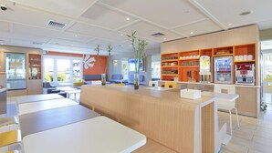 Una cafetería moderna con zonas de estar, una máquina de café y una vitrina con tazas y platillos.