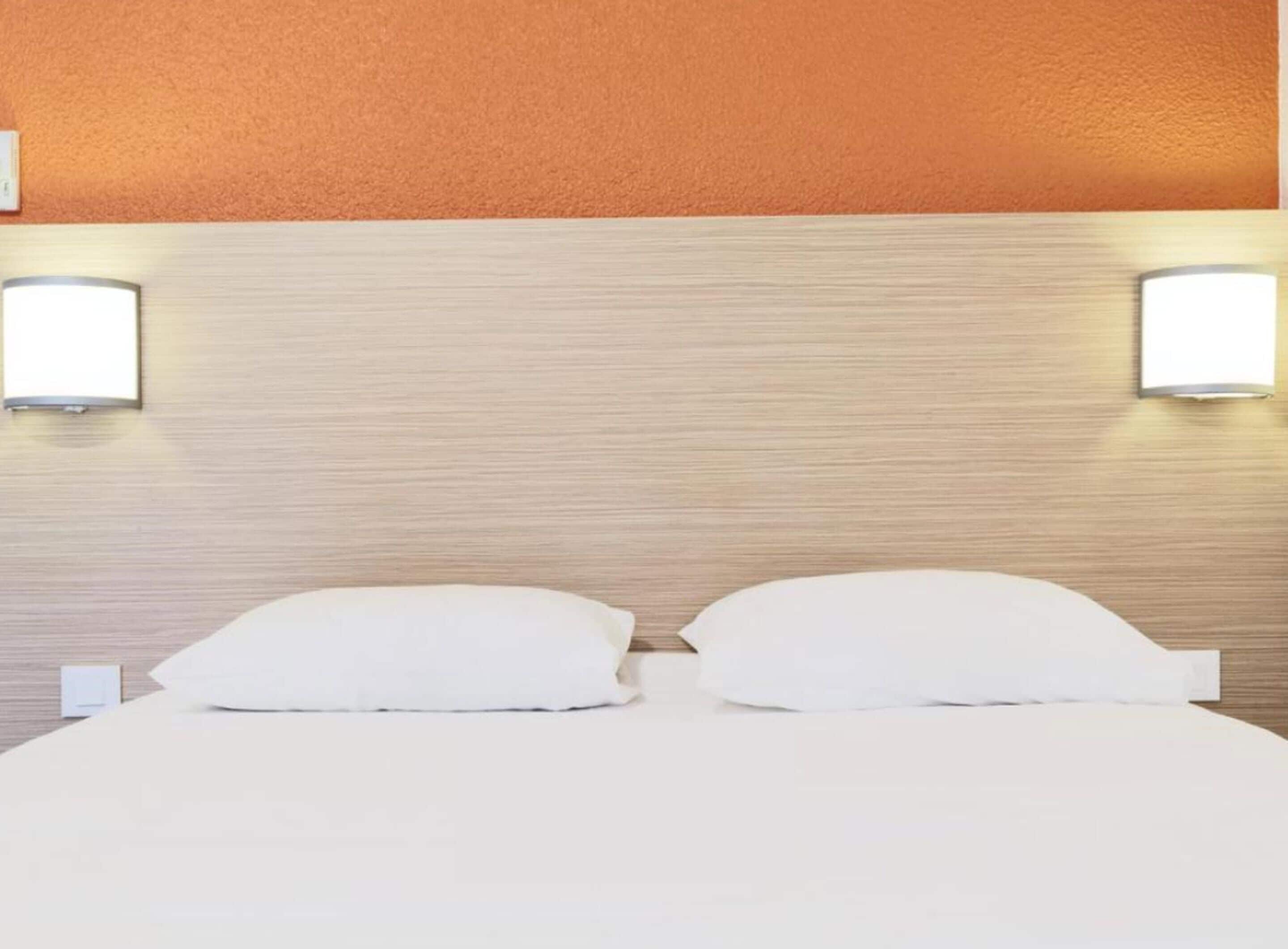 A hotel room with a wooden headboard, two bedside lamps, and a neatly made bed with white linens.