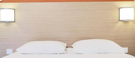 A hotel room with a wooden headboard, two bedside lamps, and a neatly made bed with white linens.