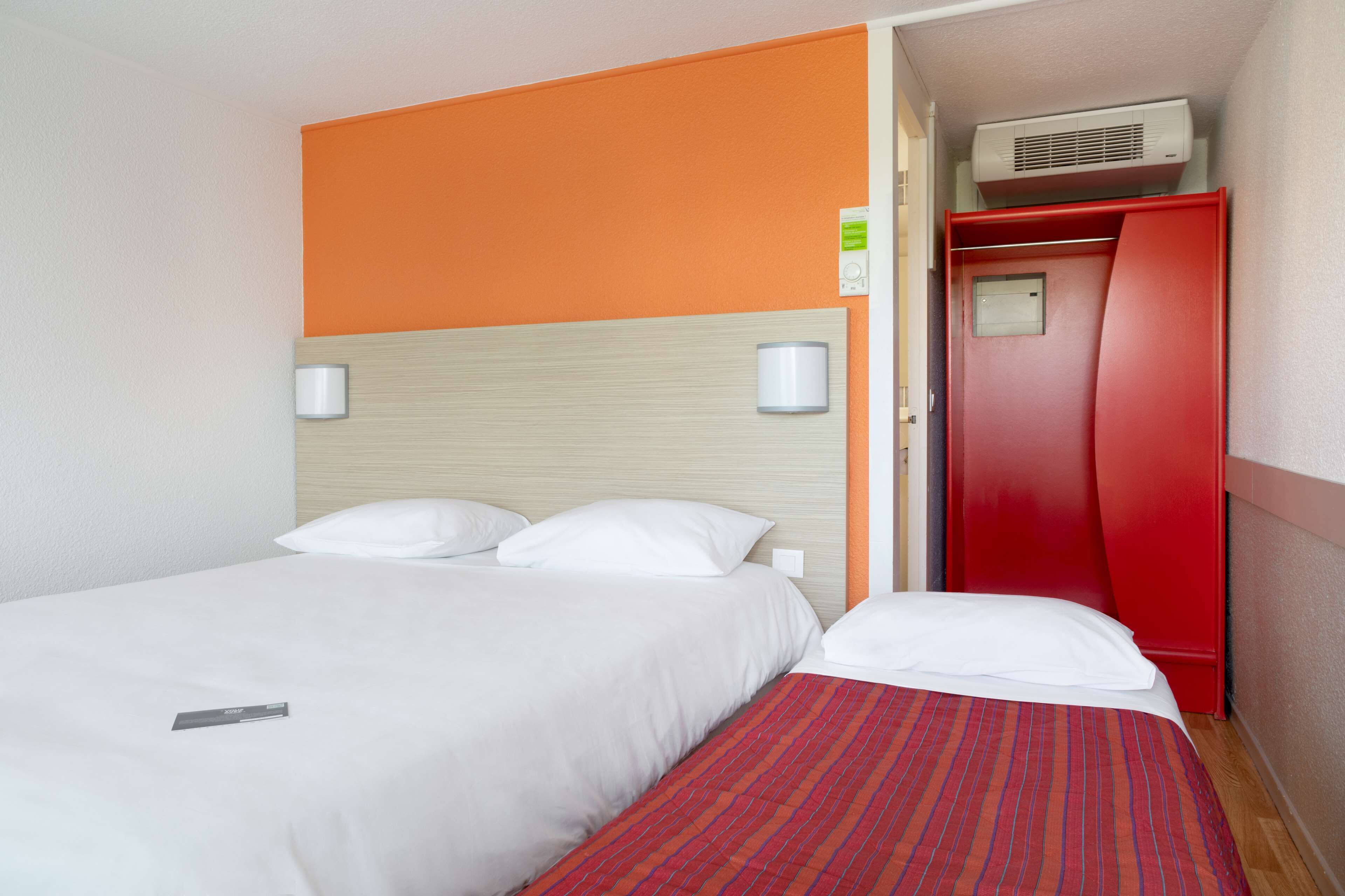 Une chambre d’hôtel avec un lit, une armoire rouge et un climatiseur fixé au mur.