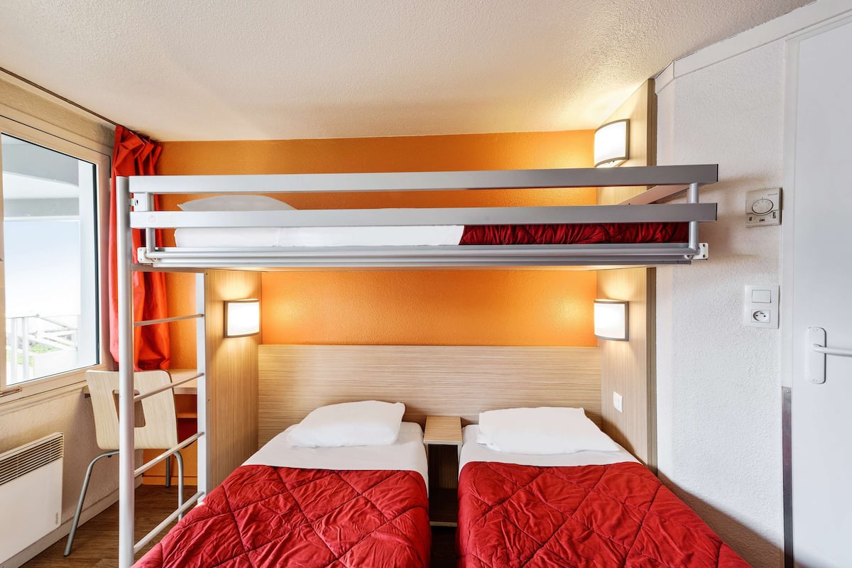 A compact room with bunk beds, a desk, and a window with curtains.