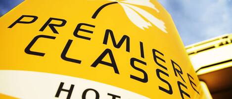Una señal amarilla con la inscripción 'PREMIERE CLASSE HOTELS' y un símbolo blanco de fleur-de-lis.