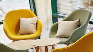 Un interior moderno con tres sillones en amarillo y verde, una pequeña mesa de madera y una vista a través de un ventanal grande.