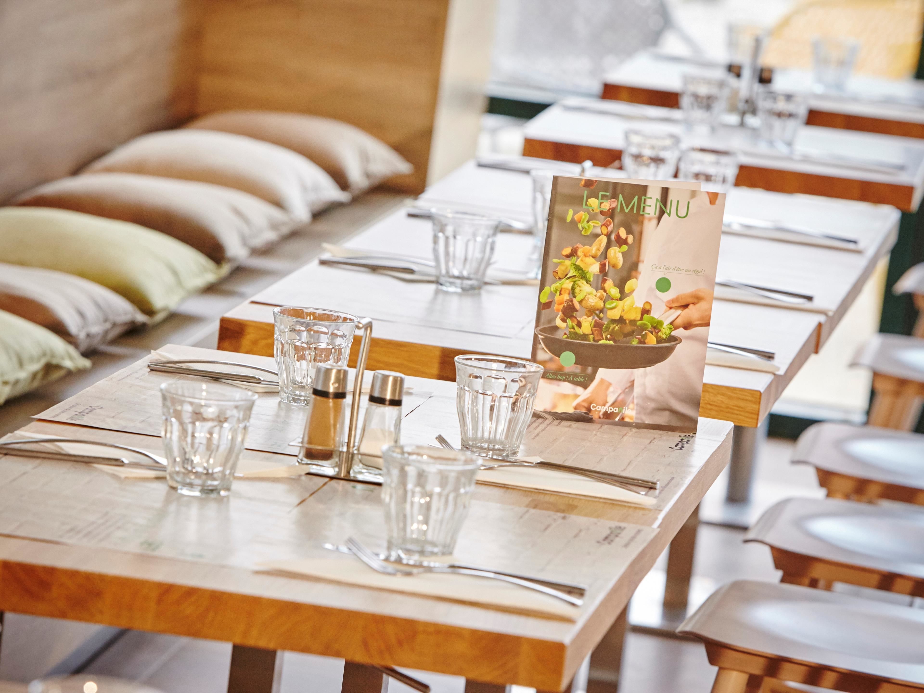 Een restaurant met netjes opgemaakte tafels, elk voorzien van bestek, glazen en een menukaartstandaard.