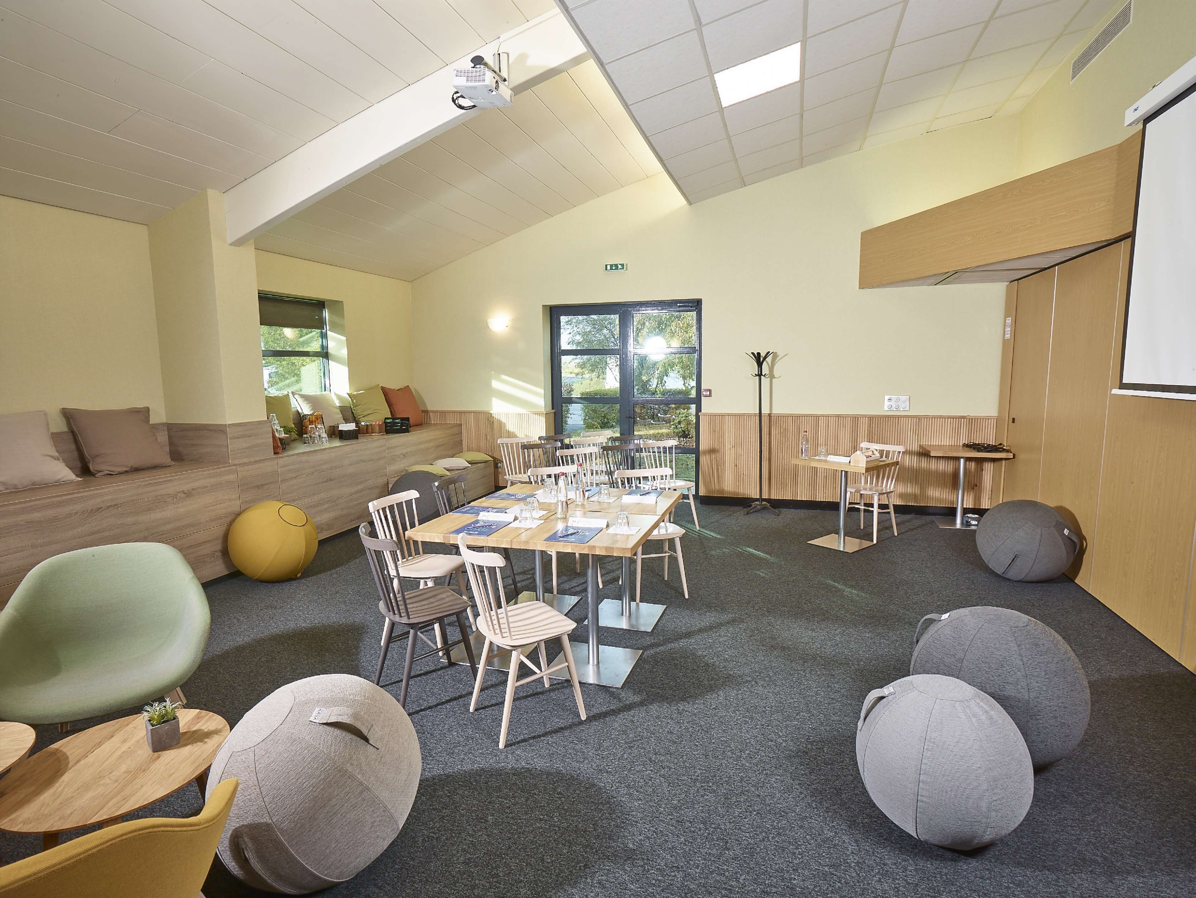 A conference room with a long table, chairs, and a projector. There are bean bags and a sofa in the corner.