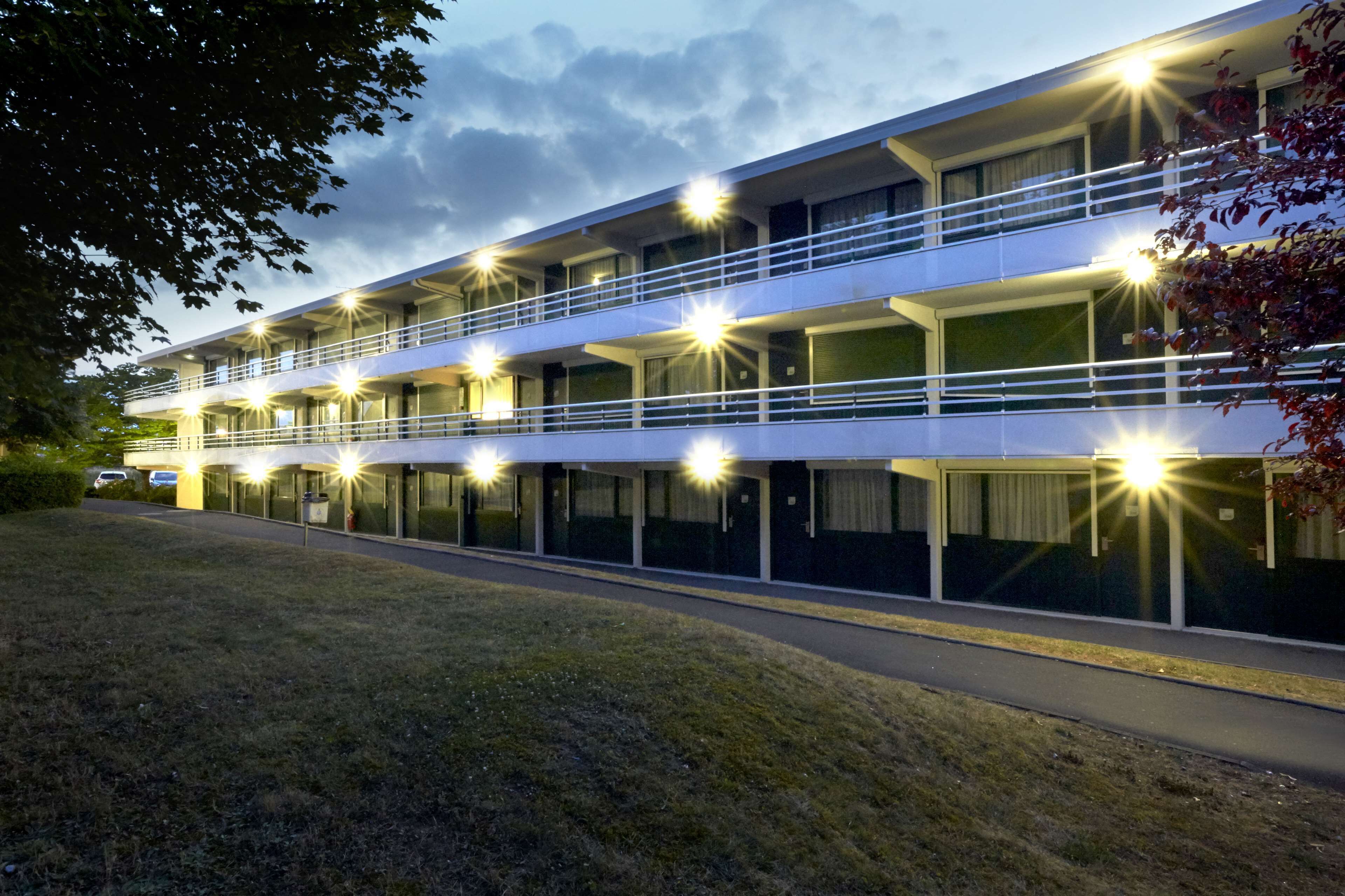 Un hotel de varios pisos con un diseño moderno, con balcones y un estacionamiento.