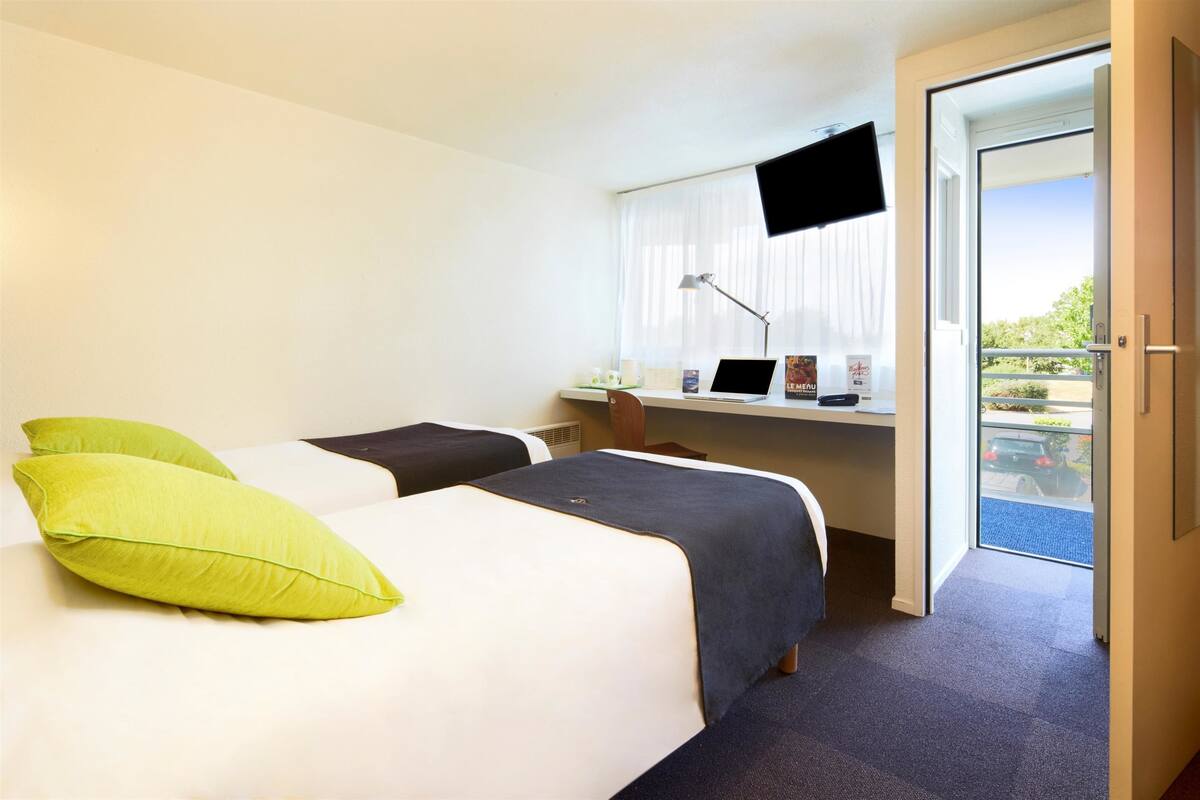Habitación de hotel con dos camas, un escritorio con una computadora portátil, un televisor y un balcón con vistas.