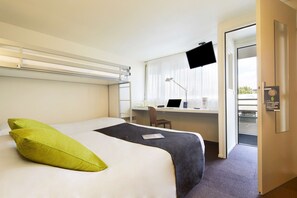 Una habitación de hotel con una cama, un escritorio con una computadora portátil, una silla y un televisor montado en la pared.