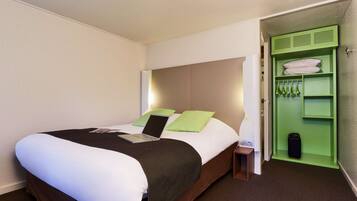 Een hotelkamer met een bed, een laptop, een groene muur en een opbergmeubel met daaraan hangende spullen.