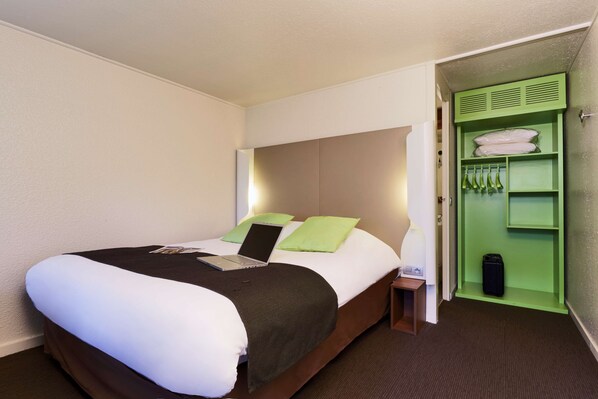 Habitación de hotel con cama, laptop, pared verde y un armario con objetos colgando.