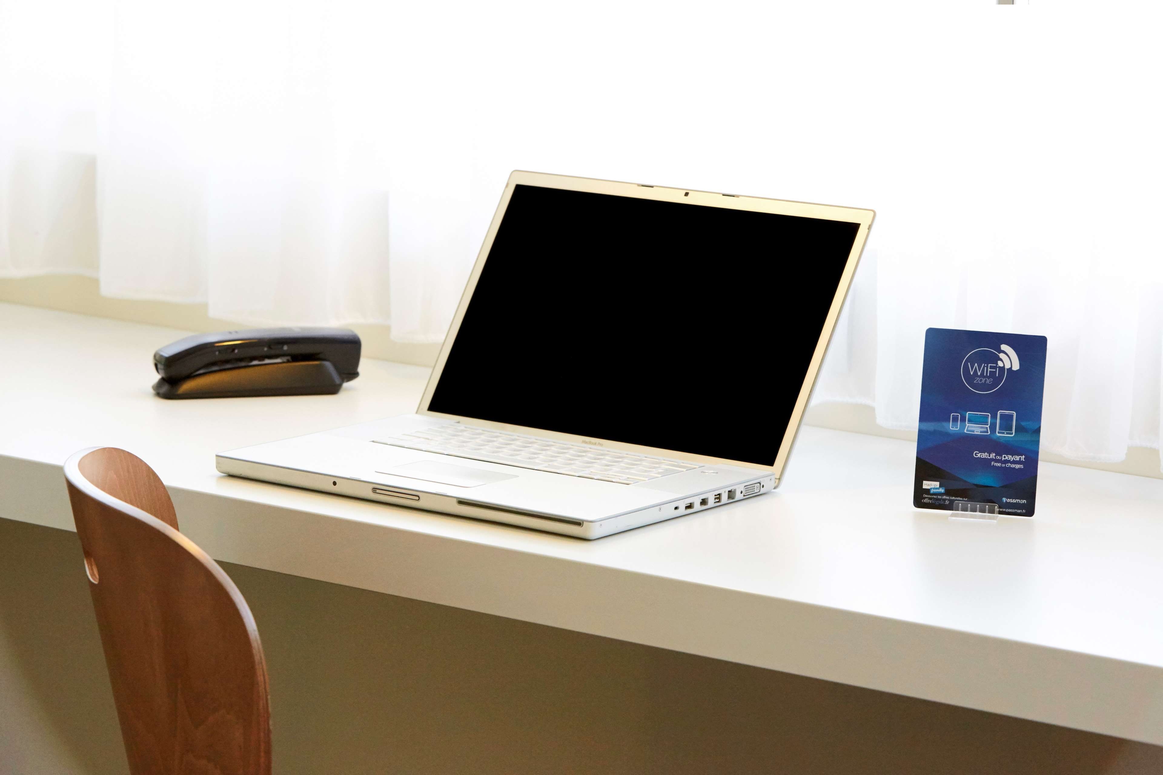 A laptop on a desk with a mobile phone and a WiFi zone sign.