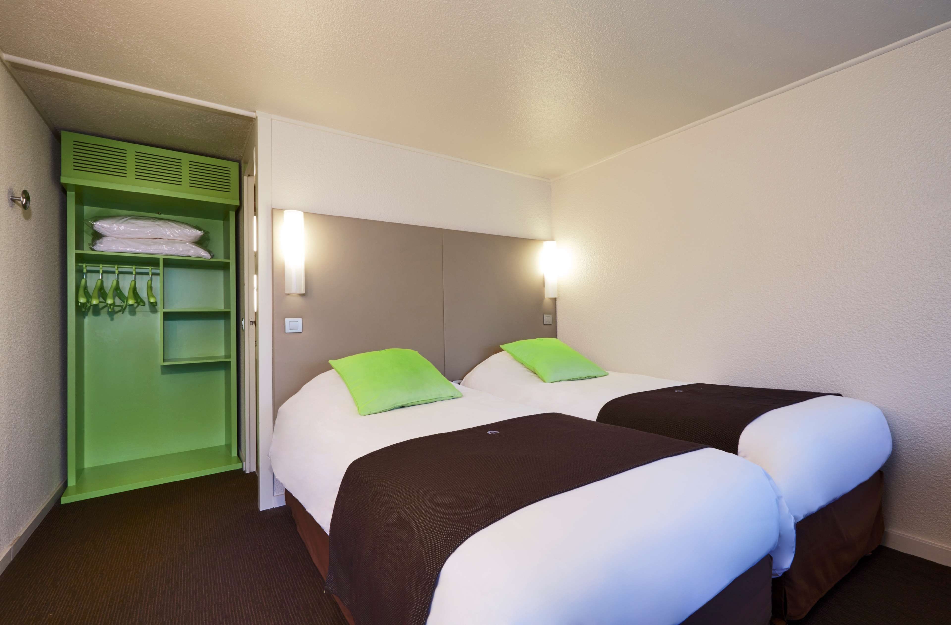 Une chambre d’hôtel avec deux lits, une armoire verte et un luminaire fixé au mur.
