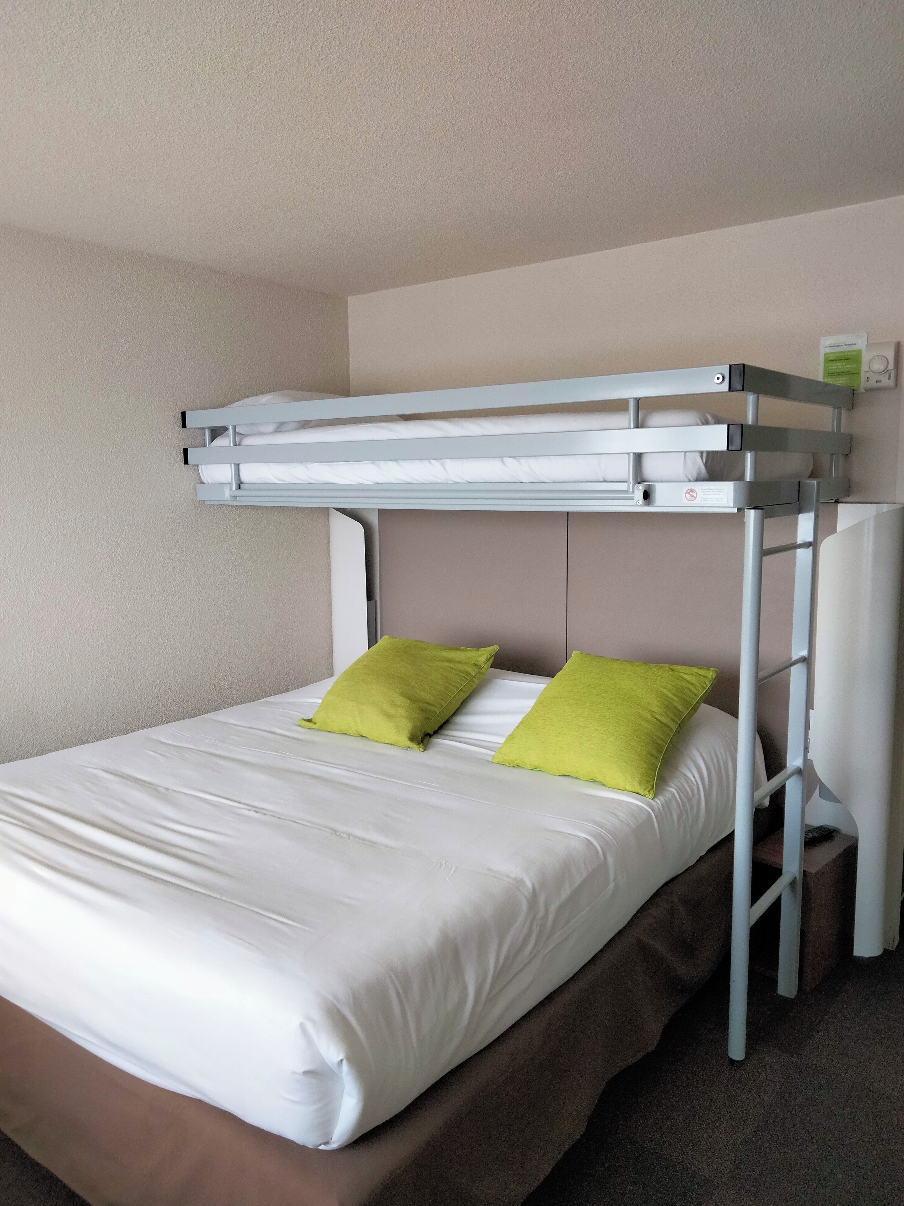 A bunk bed with white bedding and green pillows, a white headboard, and a small bedside table with a lamp.