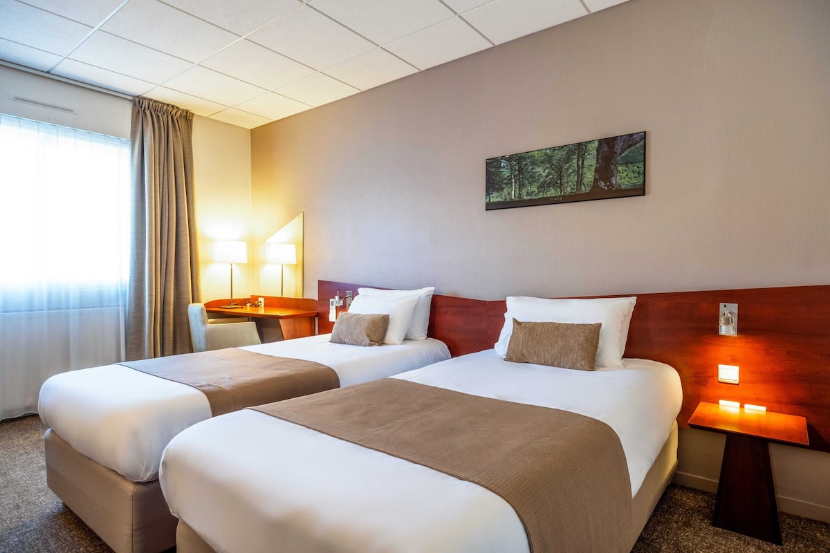 Une chambre d’hôtel avec deux lits, un bureau, une chaise, une lampe et un tableau au mur.