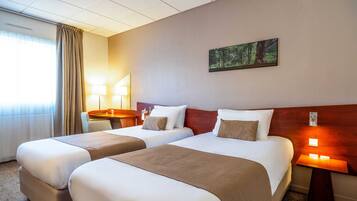 A hotel room with two beds, a desk, a chair, a lamp, and a painting on the wall.