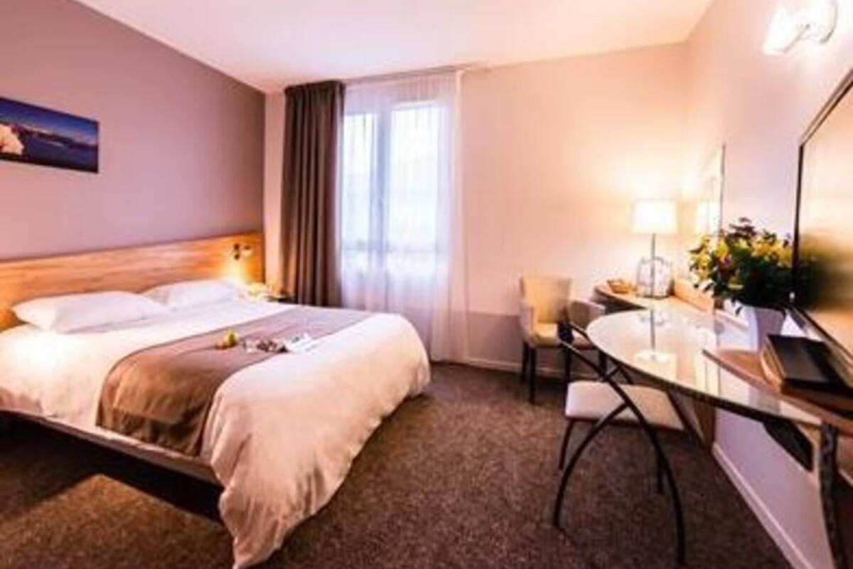 Une chambre d’hôtel avec un lit, un bureau, une chaise et une fenêtre avec des rideaux.