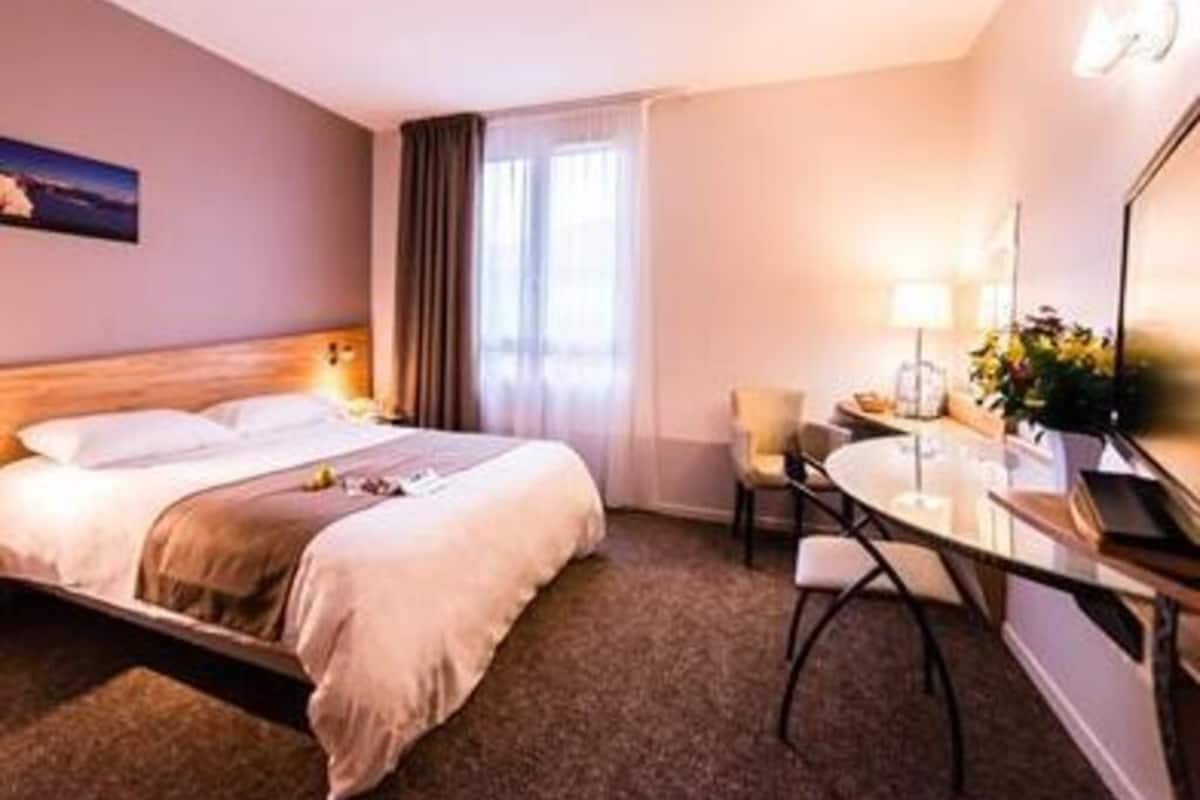 A hotel room with a bed, a desk, a chair, and a window with curtains.