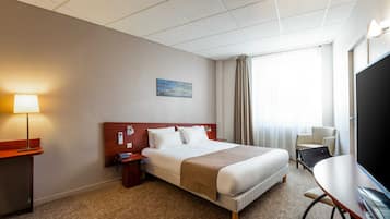 A hotel room with a large bed, a desk with a chair, a lamp, a TV, and a painting on the wall.