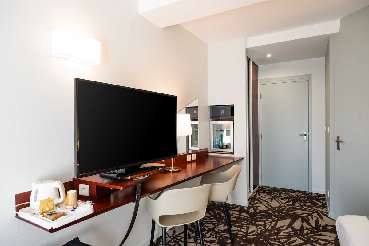 Une chambre d’hôtel équipée d’une télévision, d’un bureau, d’une chaise, d’une petite table avec une bouilloire, une tasse et un plateau avec des en-cas.