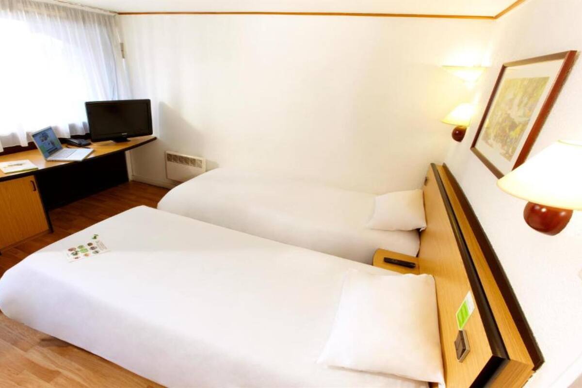 Et hotelværelse med to senge, et skrivebord med computer, fjernsyn og lampe.