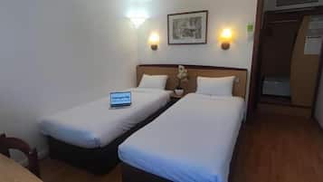 A hotel room with two single beds, a bedside table with a lamp, a small potted plant, and a sign indicating the room type.