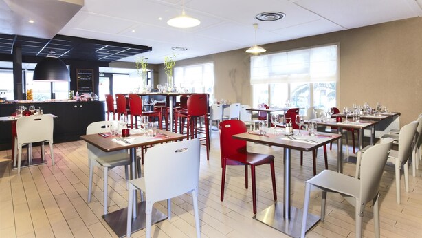 A modern restaurant with tables and chairs, a bar area, and large windows allowing natural light. - Campanile Perpignan Sud (Perpignan)