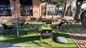 An outdoor seating area with tables and chairs, a Heineken sign, and a building with large windows. - Campanile Perpignan Sud (Perpignan)