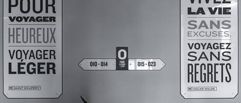 Tres letreros en una pared: uno con una cita de Saint Exupery, otro con una cita de Oscar Wilde, y un cartel direccional con los números 010-014 y 015-023.
