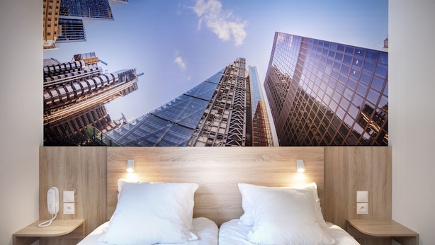 Habitación de hotel con amplia vista panorámica de la ciudad, dos camas, cabeceros de madera, mesitas de noche con lámparas y un teléfono.