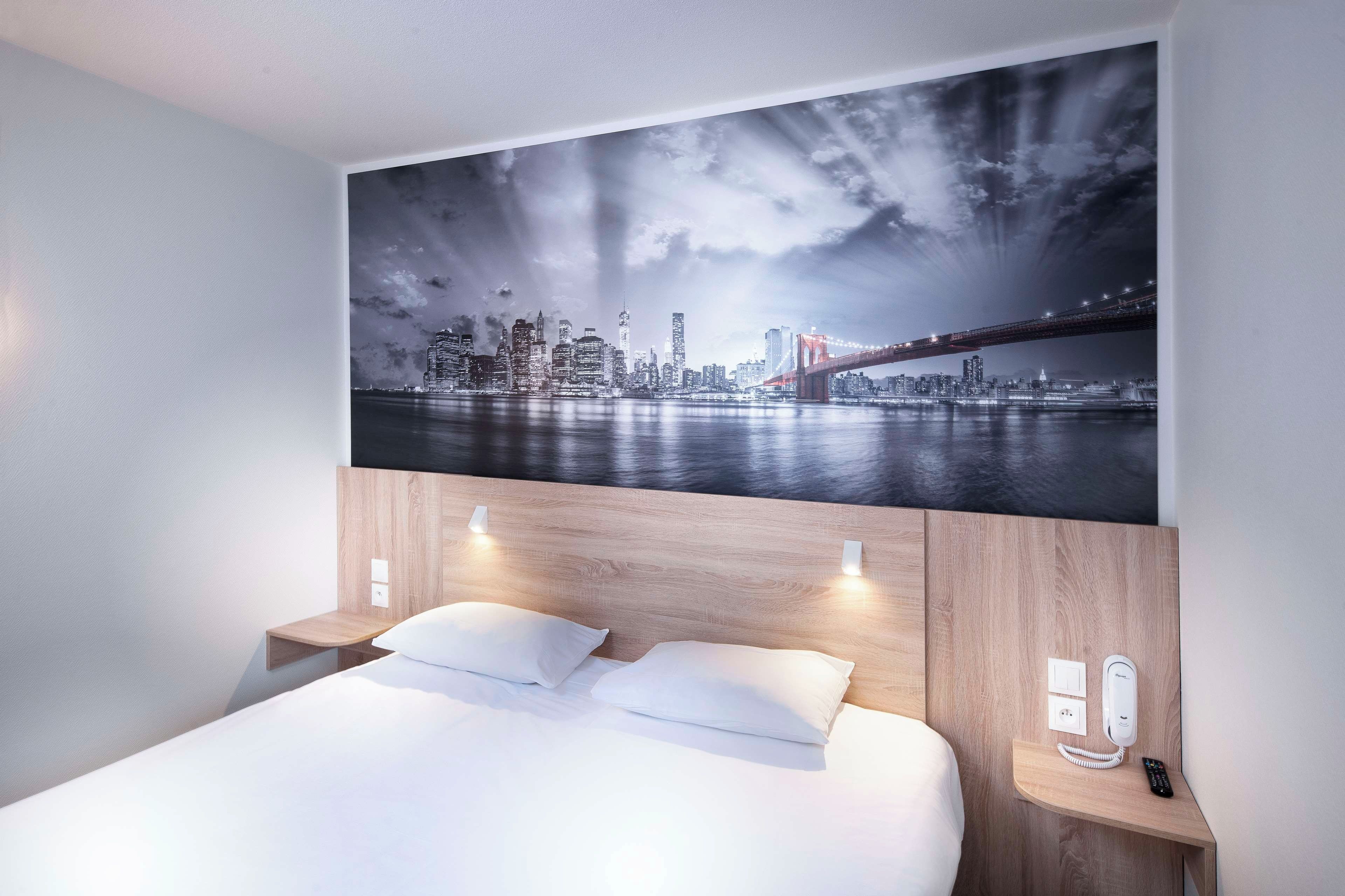 Ein Hotelzimmer mit einem großen Bett, zwei Nachttischen, einem an der Wand befestigten Telefon und einem Stadtbild.