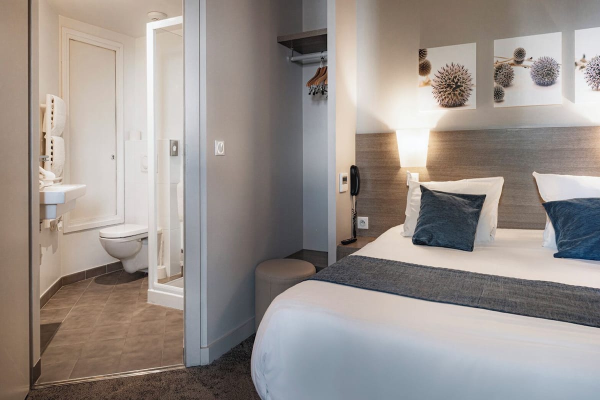 A hotel room with a bed, bedside table, lamp, and artwork on the wall.