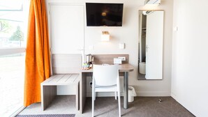 Habitación de hotel con escritorio, silla, televisor, espejo y aire acondicionado.