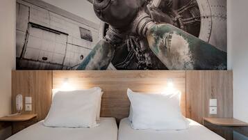 Hotelkamer met een groot muurschildering van industriële machines, een houten hoofdbord en twee nachtkastjes met lampen.