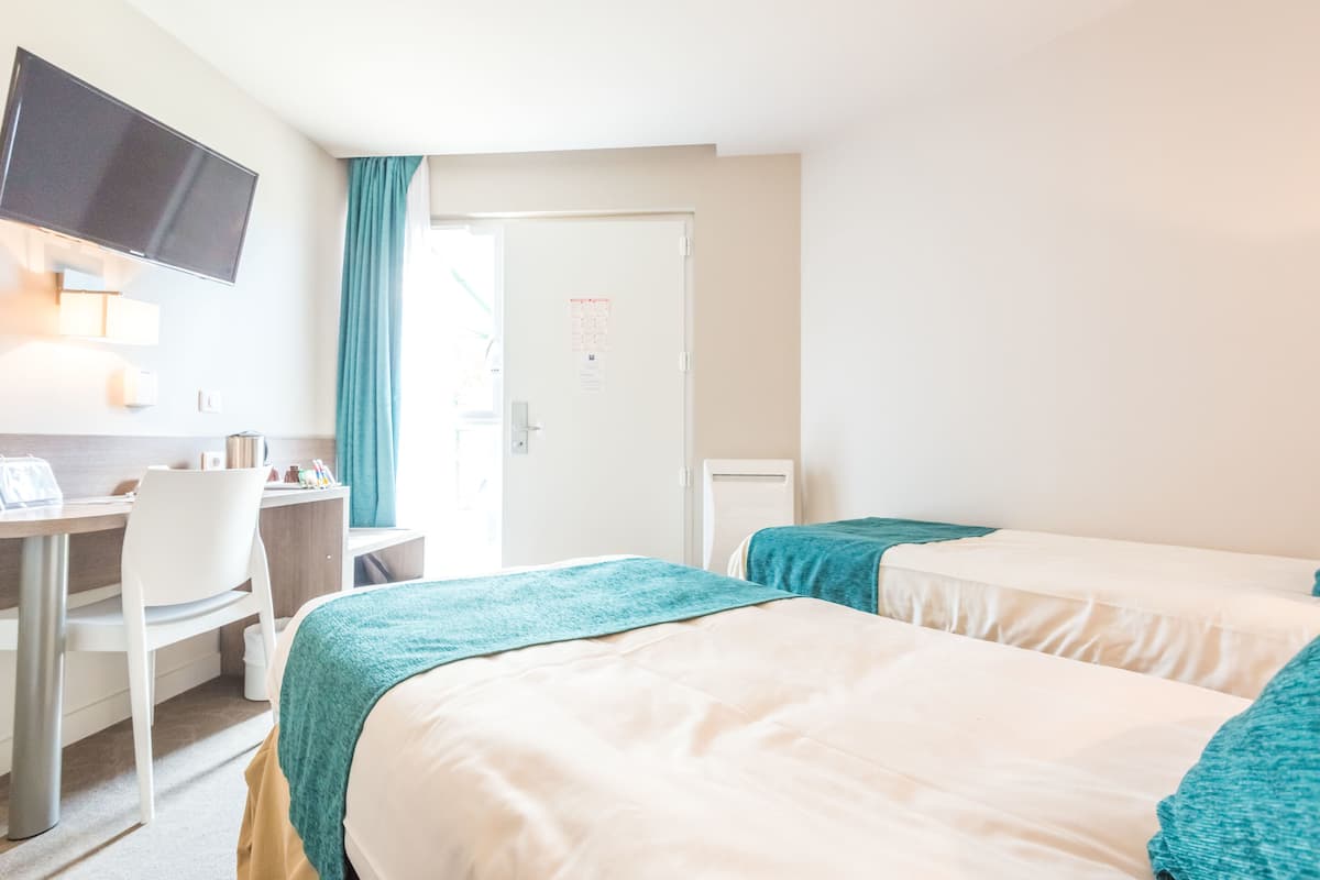 A hotel room with two beds, a desk, a chair, and a television mounted on the wall.