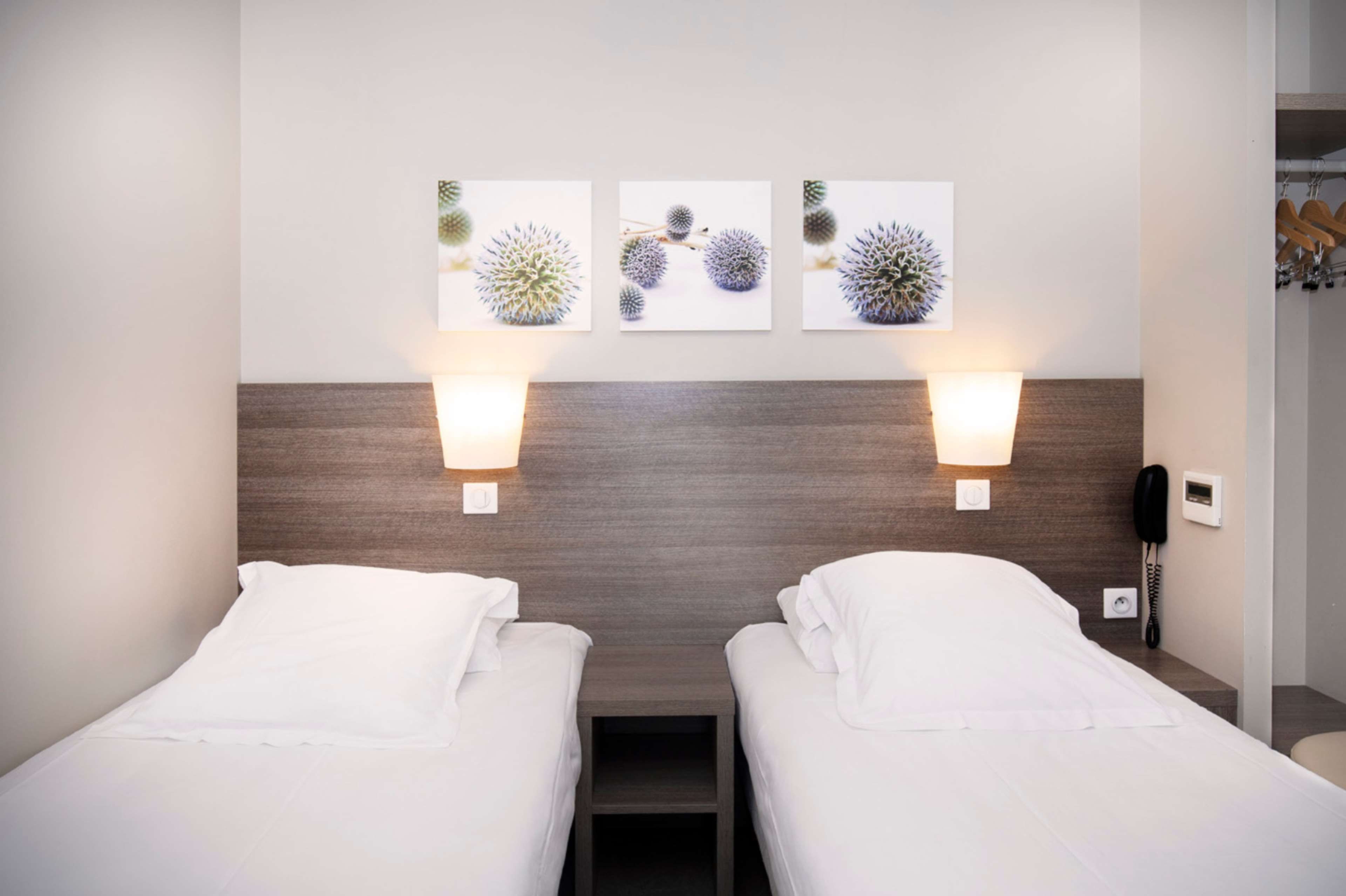 Une chambre d’hôtel avec deux lits, une tête de lit en bois, des appliques murales et un téléphone.