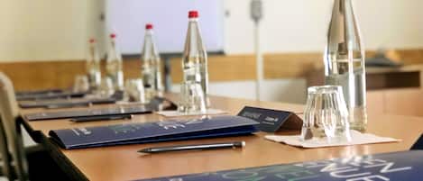 Une salle de conférence avec une longue table préparée pour une réunion, équipée de porte-noms, de bouteilles d’eau et de verres.