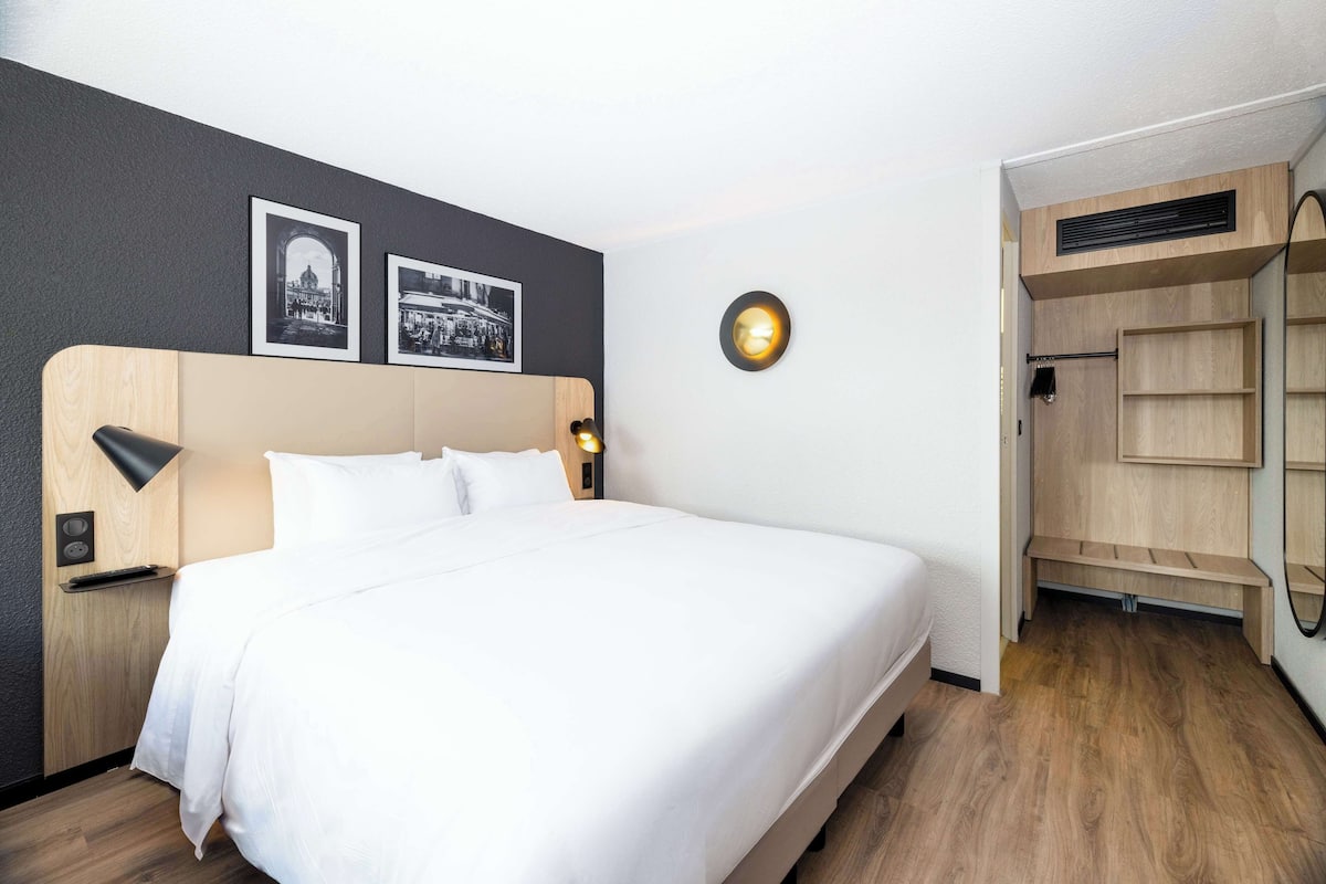 Een net opgemaakt bed met witte lakens, een hoofdbord met houten afwerking en twee wandlampen.