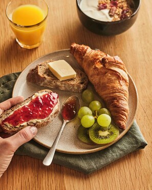 Een ontbijtbord met toast, een croissant, druiven, kiwischijfjes en een glas sinaasappelsap.