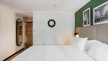A modern hotel room with a bed, a built-in wardrobe, a round light fixture, and framed pictures on the wall.