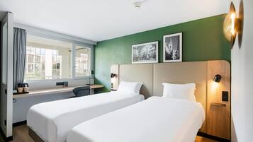 Habitación de hotel con dos camas, un escritorio, una silla, una ventana con cortinas y dos lámparas de pared.