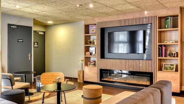 Un espace de détente moderne doté d’un téléviseur à écran plat, d’étagères en bois remplies de livres, d’une cheminée et de différents types de sièges.