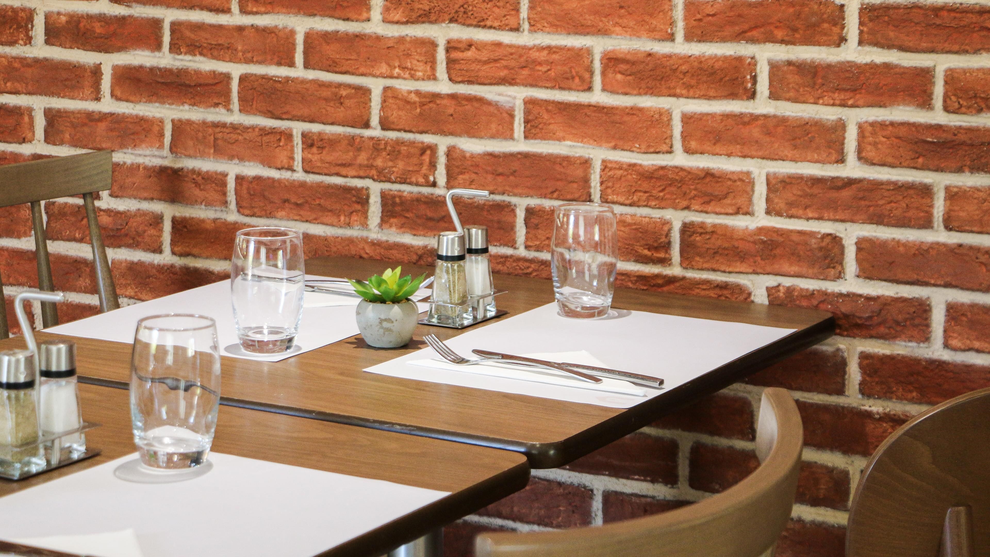 A table set with water glasses, a small plant, salt and pepper shakers, and cutlery.