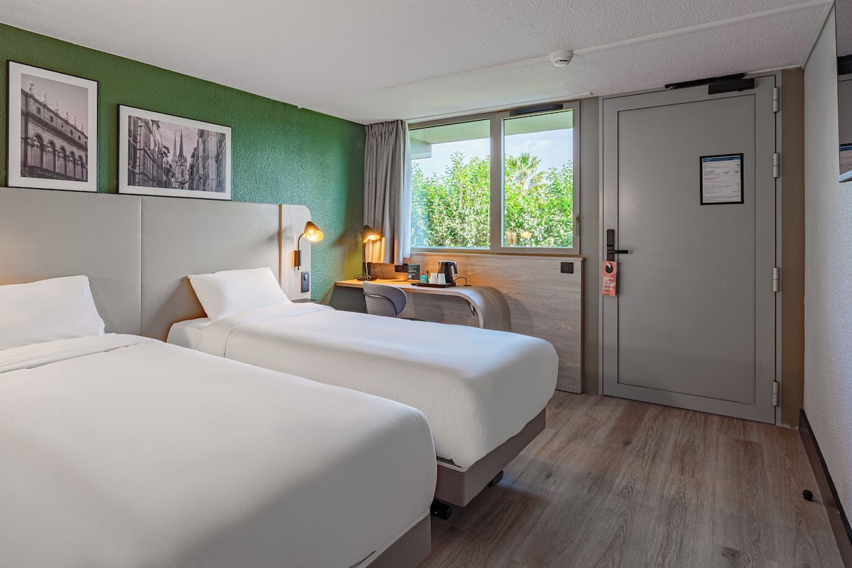 Hotelkamer met twee bedden, een bureau, een stoel, een raam met uitzicht en een deur met slot.