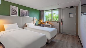A hotel room with two beds, a desk, a chair, a window with a view, and a door with a lock.